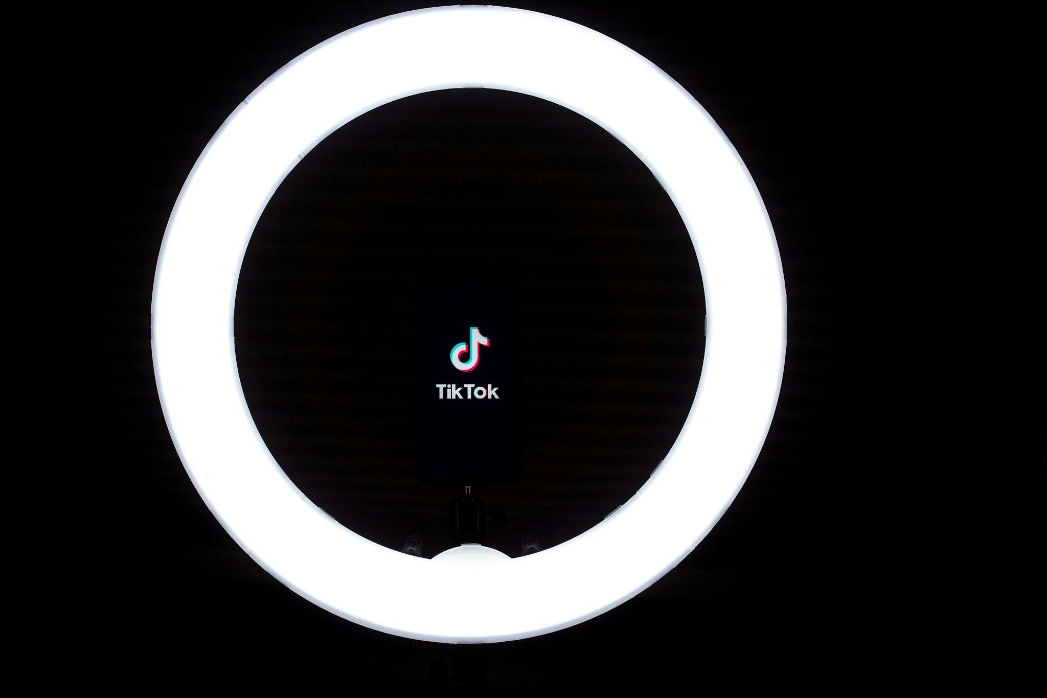 TikTok logo on a smartphone framed inside a bright ring light, representing short video content tailored to each social platform in a repurposing strategy