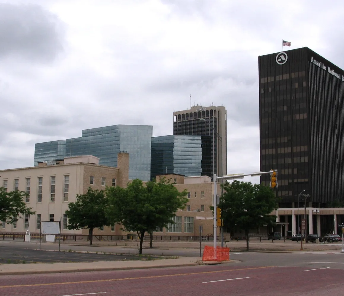 A dark bank tower and blue glass offices rise over a quiet Amarillo street under heavy grey cloud