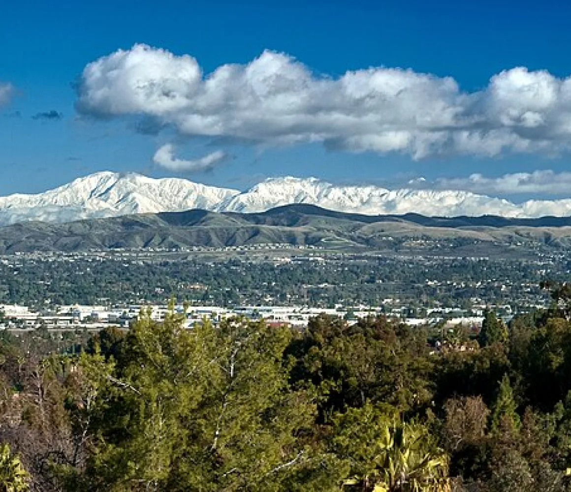Anaheim spread below snow-capped mountains, treetops and low rooftops under a bright blue sky