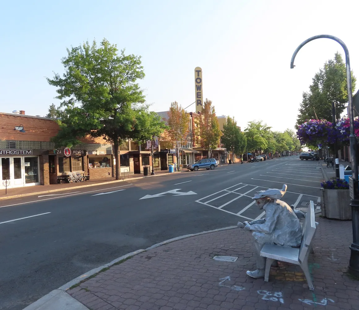 Early morning on a quiet Bend street, brick storefronts, a theatre marquee and a bench statue