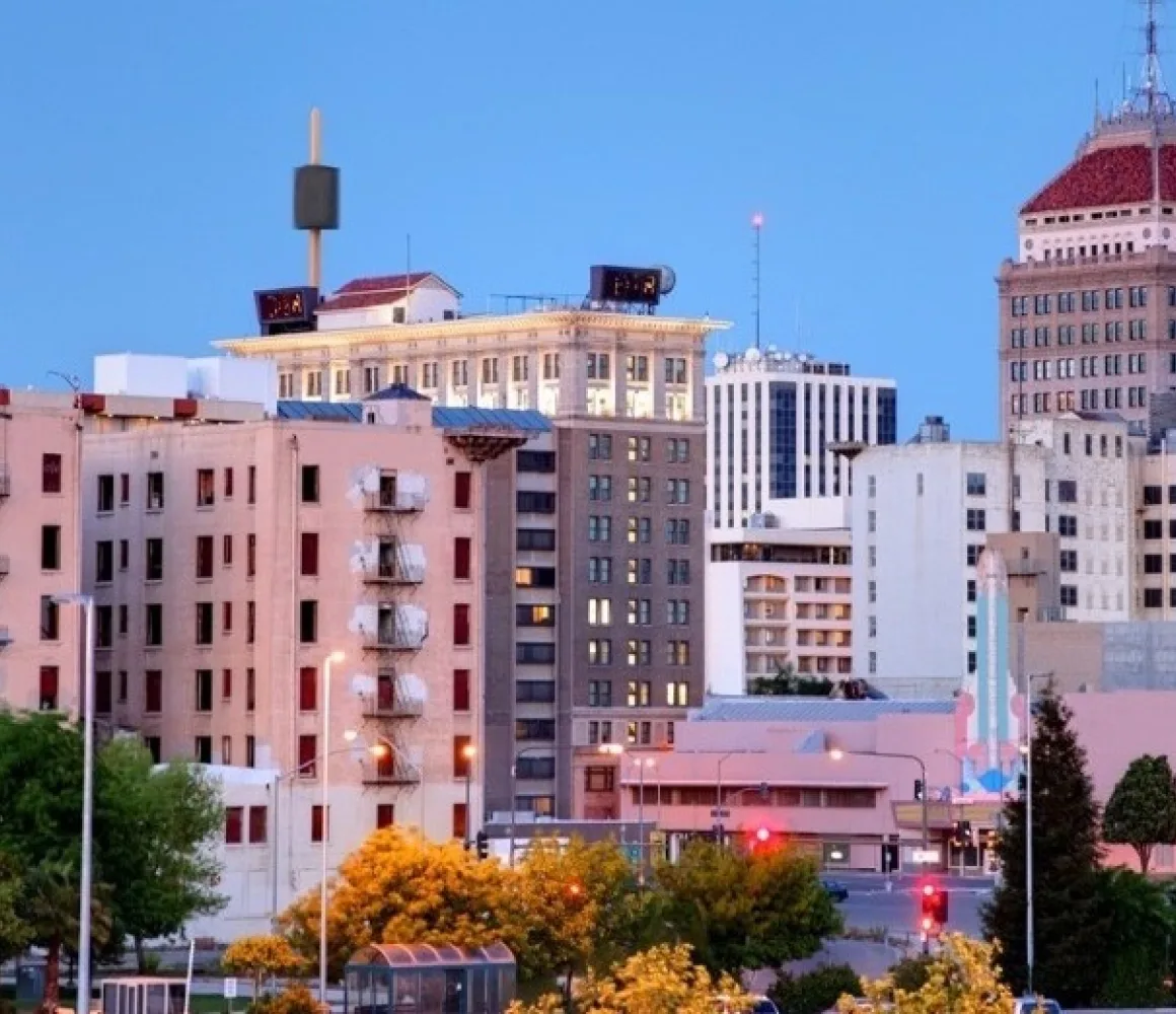 Downtown Fresno at dusk, a red-capped tower above older low-rise blocks with windows lit against blue sky