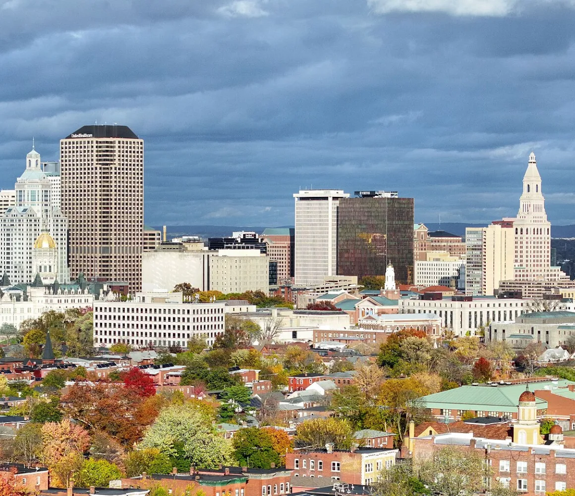 The Hartford skyline under dark storm clouds, gold-domed capitol and clock tower above autumn treetops