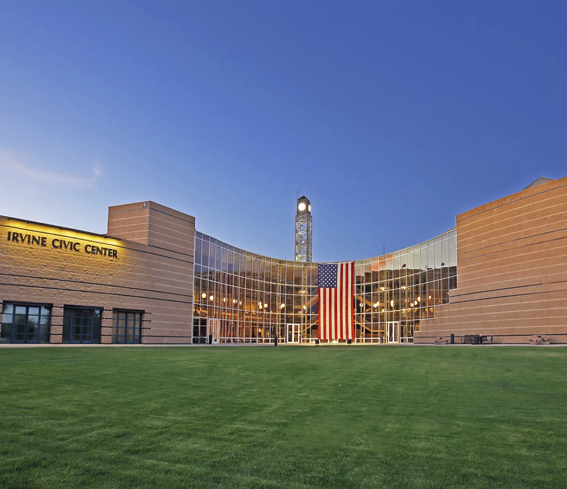 Irvine Civic Center at dusk, curved glass entrance with a large US flag and clock tower