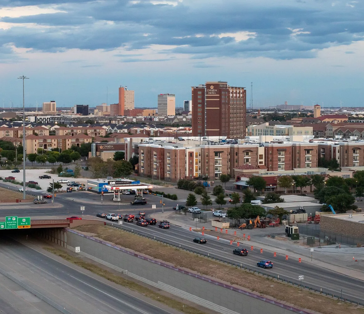 Lubbock at dusk, traffic on the freeway below brick apartments and a distant downtown skyline