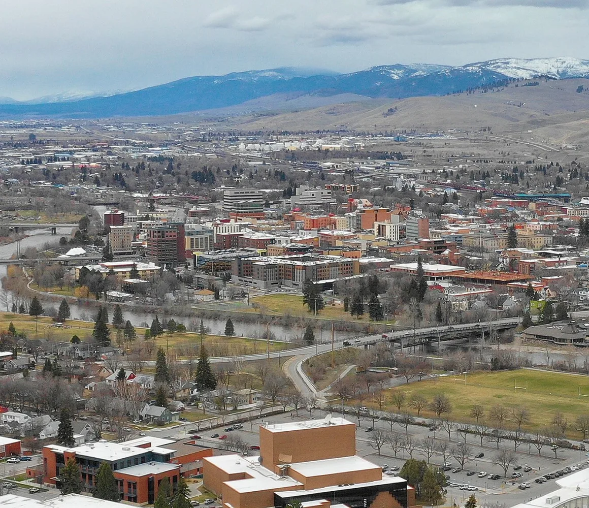 Missoula from a hillside, the river curving past downtown toward snow-dusted mountains