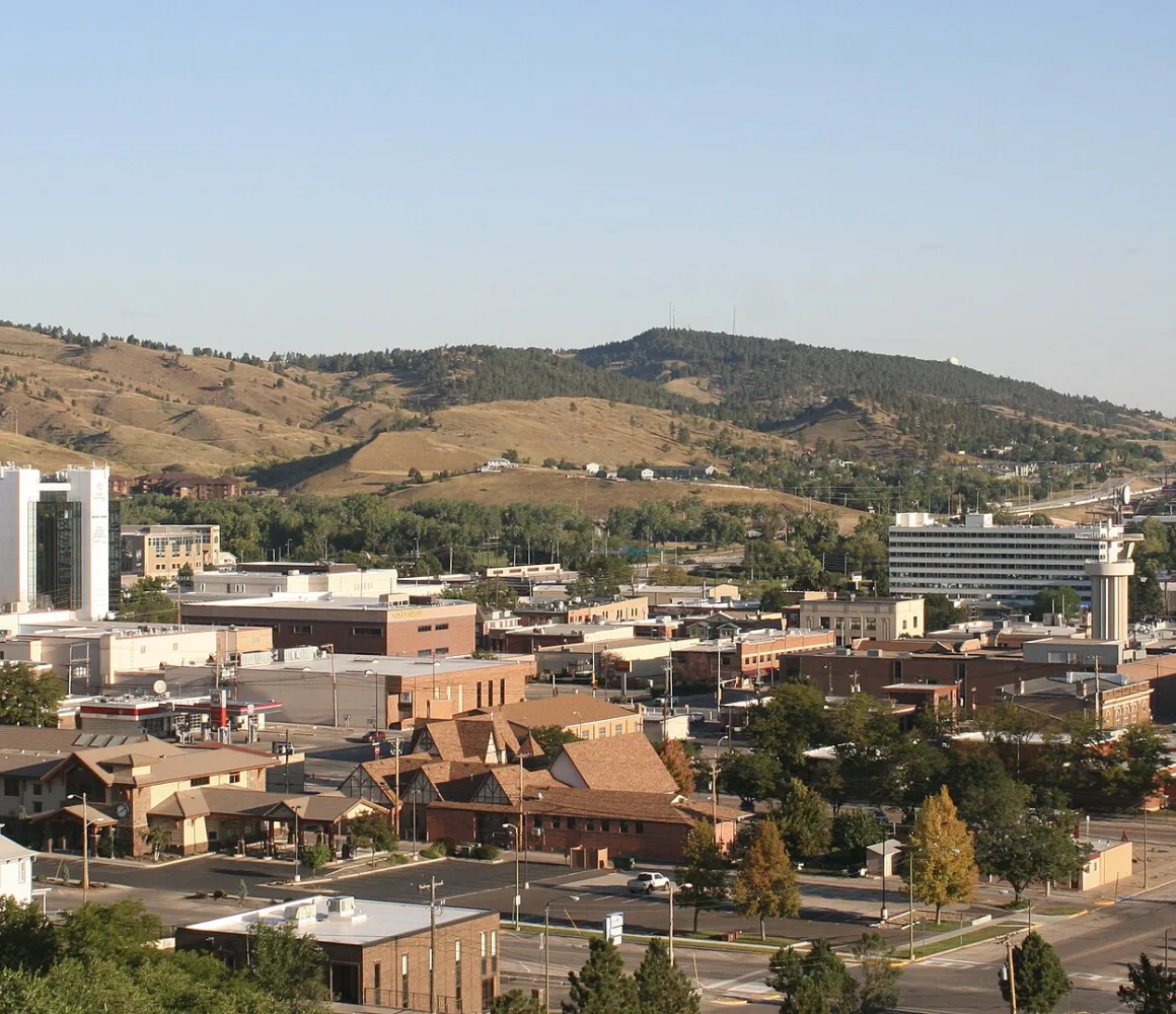 Low downtown Rapid City spread below grassy pine-dotted hills in warm late-afternoon light
