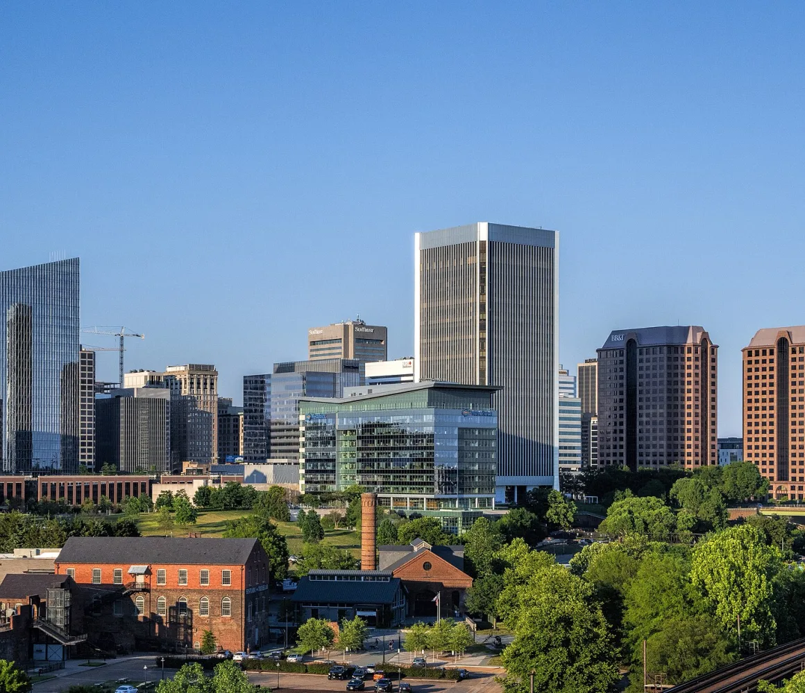 Richmond's glass and brick towers in morning sun, old warehouses and a smokestack among green trees