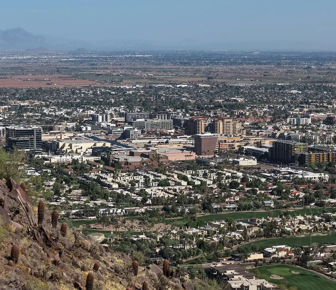 A saguaro on a rocky slope above Scottsdale, golf greens and low rooftops spreading to distant mountains