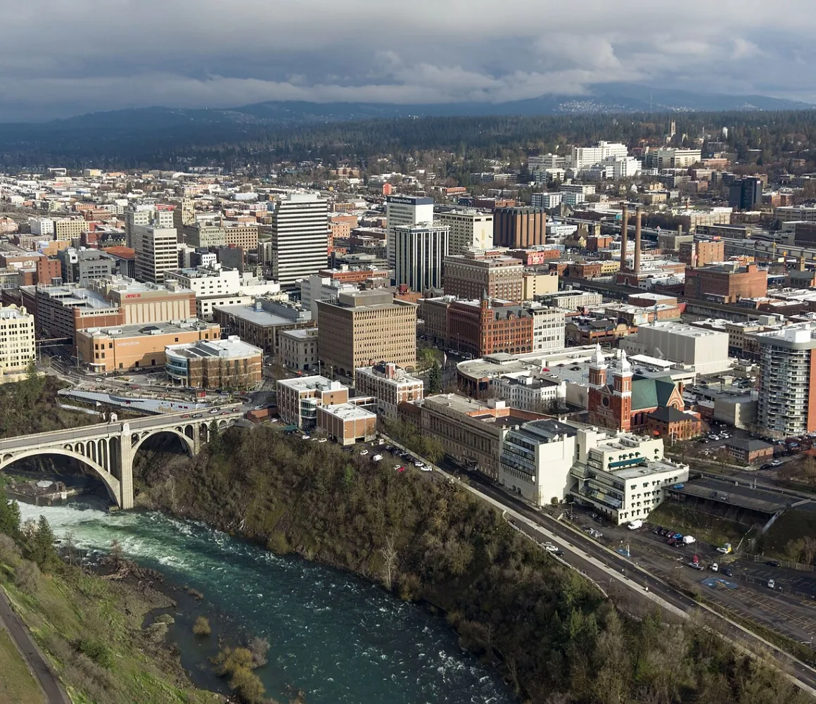 Aerial over Spokane, an arched concrete bridge above the river's rapids under a grey overcast sky
