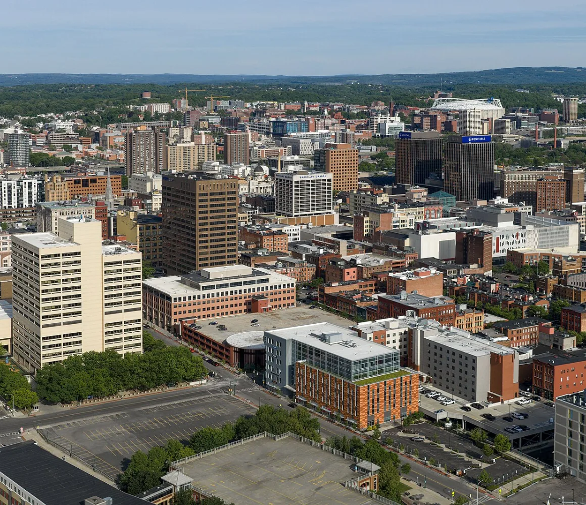 Aerial view of downtown Syracuse in summer, a white domed stadium and green hills on the horizon