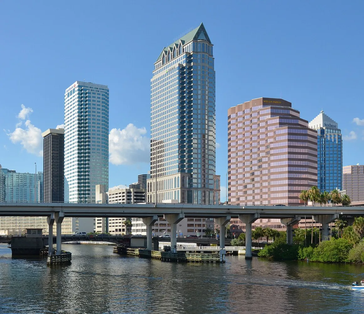 Tampa's waterfront towers and a spire-topped high-rise beyond a low bridge, small boat on the river